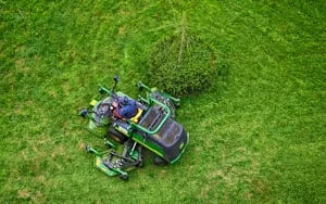 Aerial view of a zero-turn mower cutting a green lawn around a young tree
